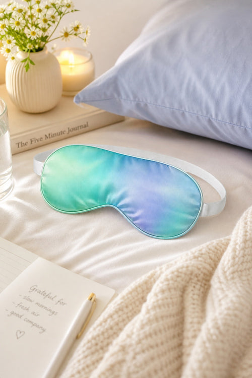 Aurora Silk Sleep Mask on a bed with soft candlelight and flowers